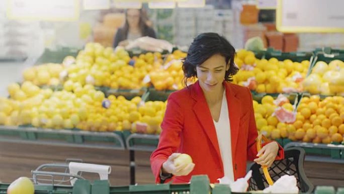在超市: 美丽微笑的女人在新鲜农产品过道中选择有机水果并将其放入购物篮的肖像。高角度拍摄。