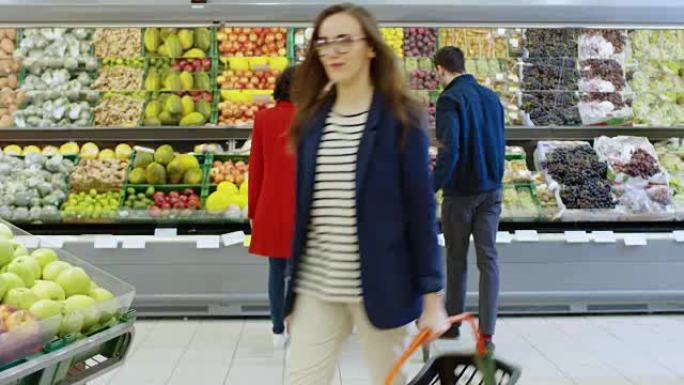 在超市: 幸福的年轻夫妇在商店的新鲜农产品区选择有机水果和浆果。男朋友推购物车，而女朋友拿水果。