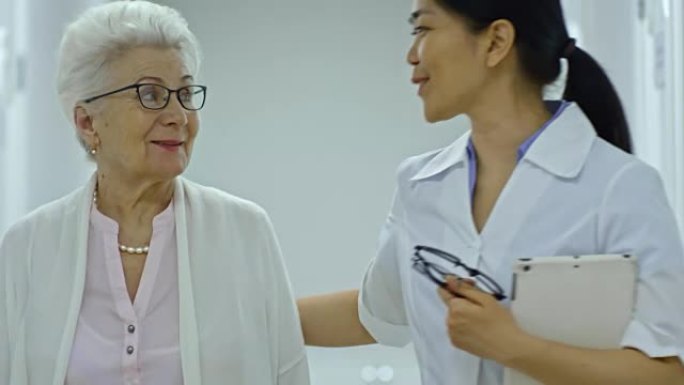 Joyous Female Doctor Walking with Senior Woman in 