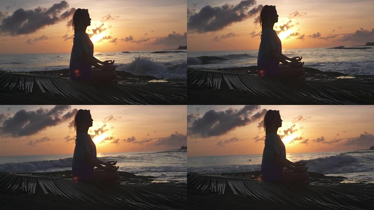 海滩上的瑜伽。以莲花姿势冥想的女人。日落