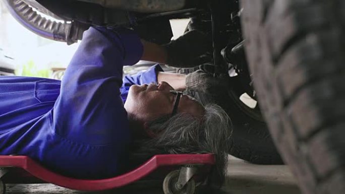 专业的男机械师躺在汽车下面，在车库里修理它。汽车服务理念。多莉开枪
