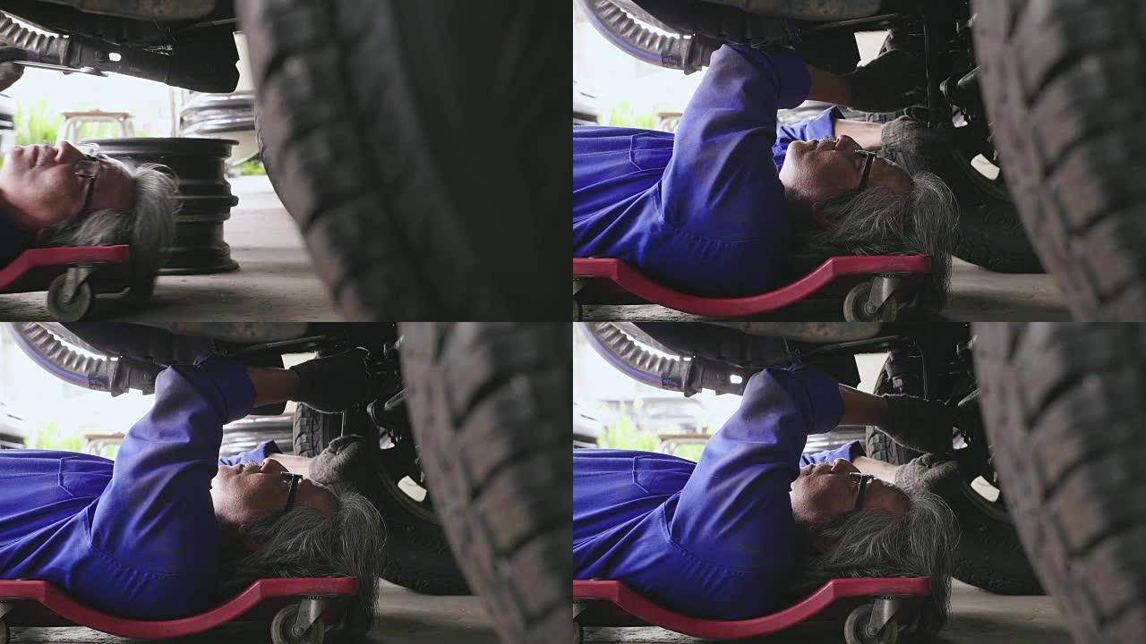 专业的男机械师躺在汽车下面，在车库里修理它。汽车服务理念。多莉开枪