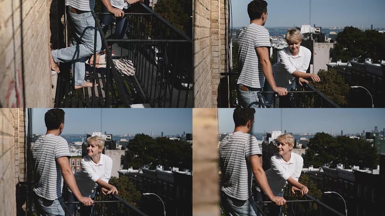 年轻的多种族浪漫夫妇站在一起，在一个阳光明媚的小阳台上聊天，可以看到令人惊叹的纽约景色