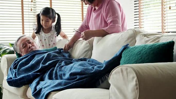 在家中的泰国家庭: 老年，休息，舒适和人的概念-老人在家睡在沙发上。这个女孩高兴地亲吻她的祖父。