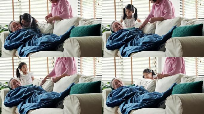 在家中的泰国家庭: 老年，休息，舒适和人的概念-老人在家睡在沙发上。这个女孩高兴地亲吻她的祖父。