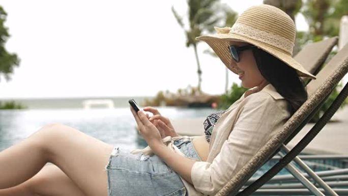 轻松的亚洲年轻女子在度假游泳池里看手机