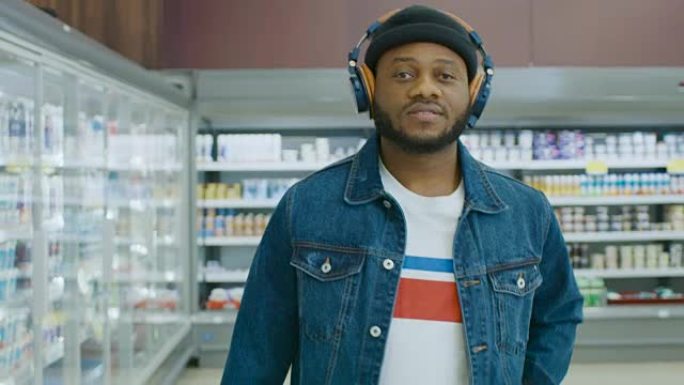 在超市: 戴着耳机的时尚非洲裔美国人走过商店的冷冻商品区。后视图拍摄。慢动作。
