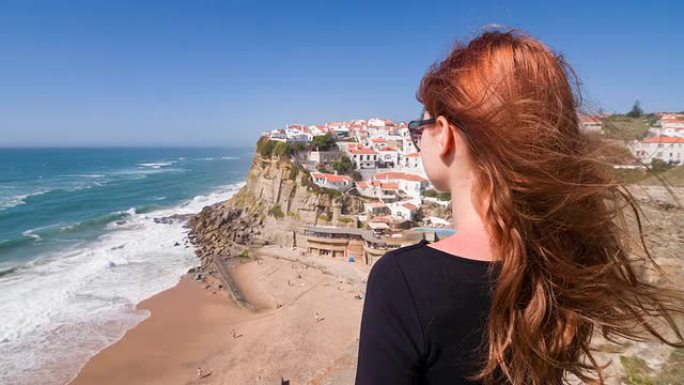 年轻的女性游客俯瞰海边陡峭悬崖上的村庄