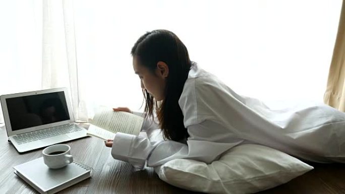 年轻女子躺在家里的地板上阅读和学习，生活方式概念，4K(UHD)