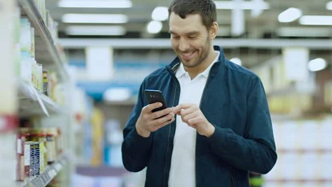 在超市: 英俊的男人使用智能手机，站在罐头食品区时微笑。