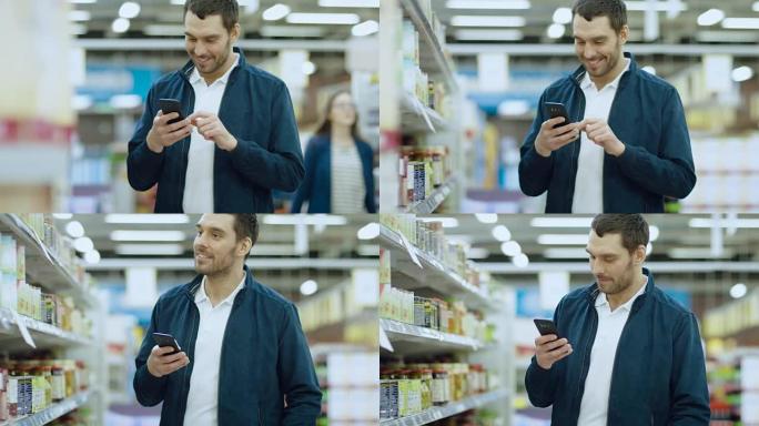 在超市: 英俊的男人使用智能手机，站在罐头食品区时微笑。