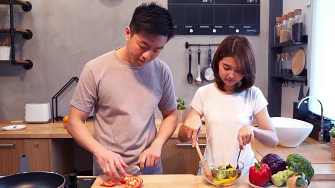 男人在厨房里切西红柿。美丽幸福的亚洲夫妇正在厨房做饭。年轻的亚洲夫妇在家里度过浪漫的时光。情侣家庭生
