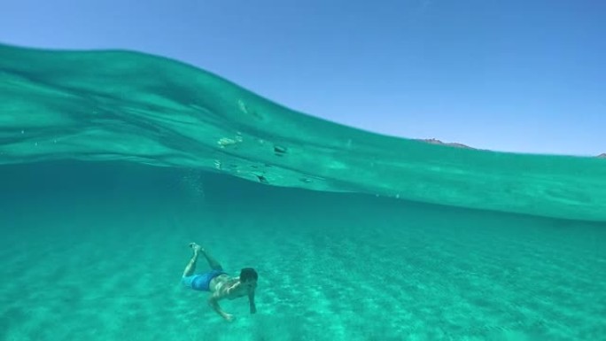 半水下: 年轻的男性游客在令人惊叹的绿松石海水中游泳。