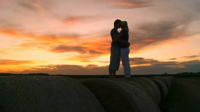 高清：日落时分情侣在干草捆上接吻