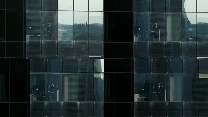摩天大楼外的航拍镜头: 商人和女商人站在办公室窗户旁谈论生意。金融商务区和在大城市工作的商人的飞行镜