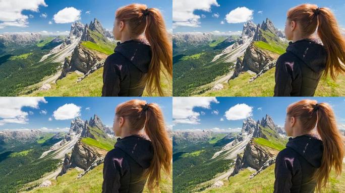 女游客站在山顶上，在美丽的晴天欣赏着她周围壮丽的山脉的景色