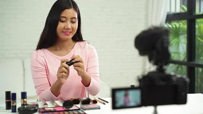 美容博客作者坐在前置摄像头录制视频时展示美容化妆品。美女在复习时使用刷子化妆教程通过互联网向社交网络