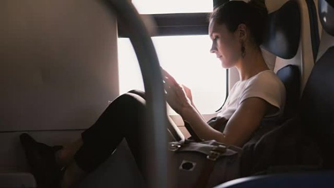 美丽自信的白人妇女在智能手机上使用信使应用程序，微笑着在火车靠窗的座位上旅行