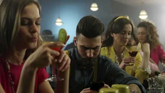 在鸡尾酒吧里，社交男子在智能手机上轻视他的朋友