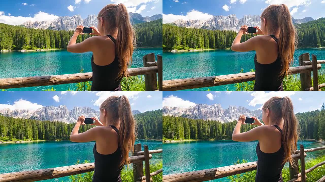 女游客探索山腰，站在湖边，群山环抱，欣赏风景，用智能手机拍照