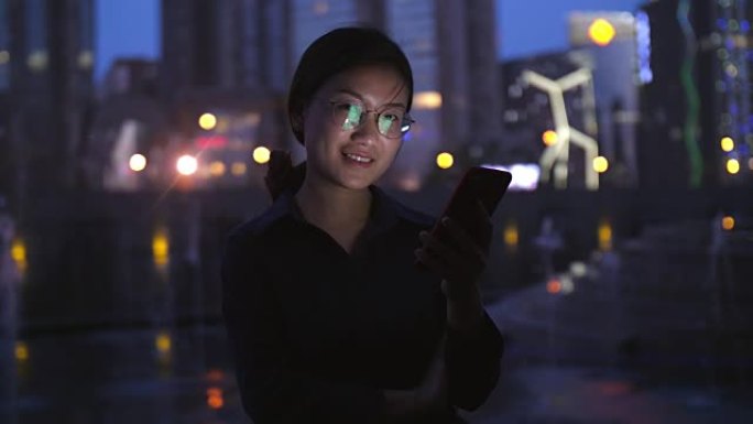 年轻的亚洲女人晚上在城里看手机，4k