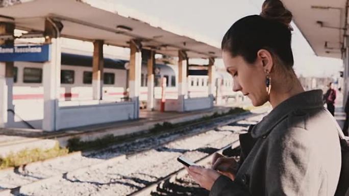 年轻的欧洲女商人在火车站的智能手机上打字信息，压力大，迟到，火车经过