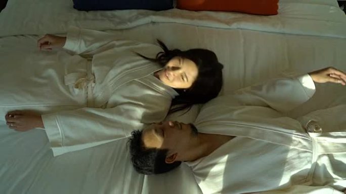 慢动作FHD镜头，恋爱中的亚洲幸福夫妇躺在床上，在豪华酒店卧室里浪漫的时刻，生活方式和休闲理念