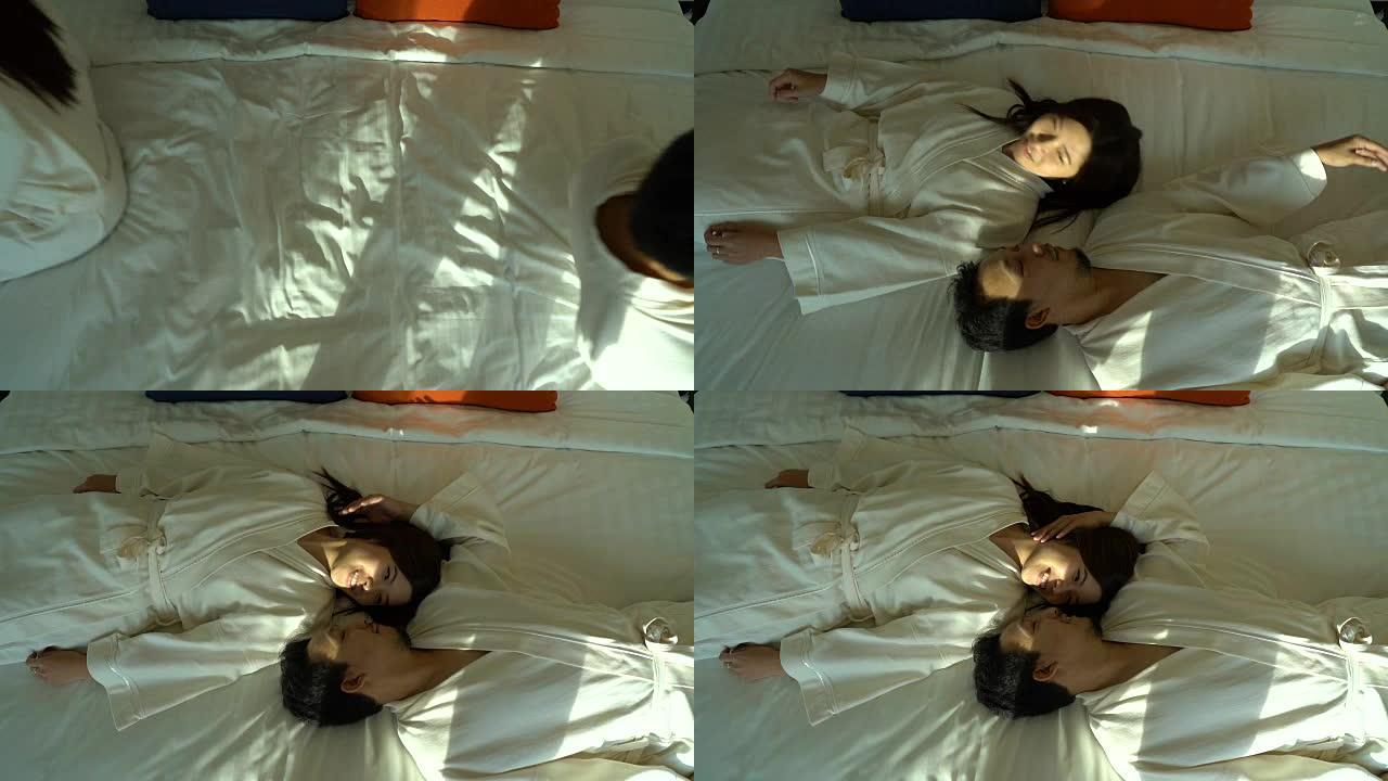 慢动作FHD镜头，恋爱中的亚洲幸福夫妇躺在床上，在豪华酒店卧室里浪漫的时刻，生活方式和休闲理念