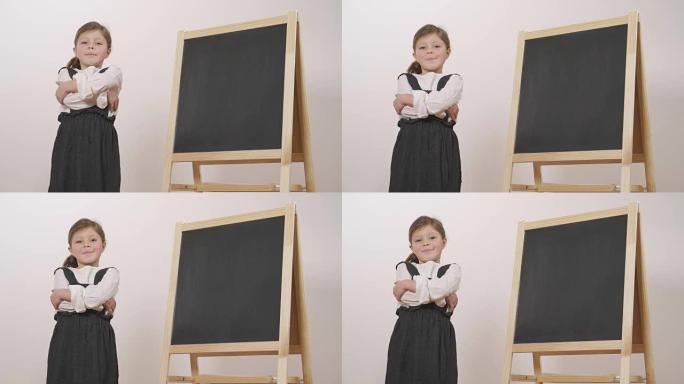 一个快乐的女孩在小黑板前打扮成老师，双臂交叉着，微笑着。