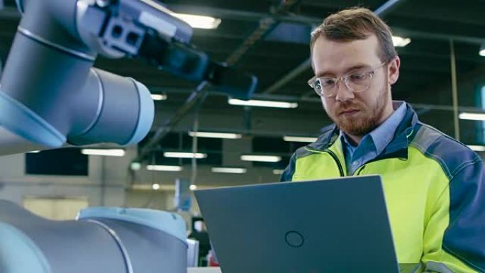 工厂手持镜头: 自动化工程师使用笔记本电脑进行编程和测试机械臂。自动制造业的新时代。