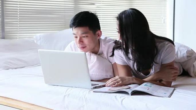 夫妇躺在床上使用笔记本电脑和阅读杂志