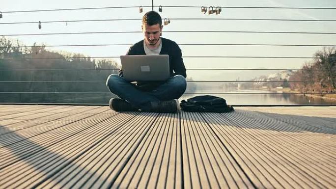 WS男子坐在桥上使用笔记本电脑