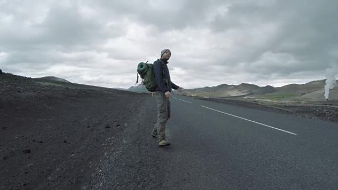 在冰岛荒凉的道路上，背着背包搭便车的游客
