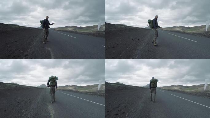 在冰岛荒凉的道路上，背着背包搭便车的游客
