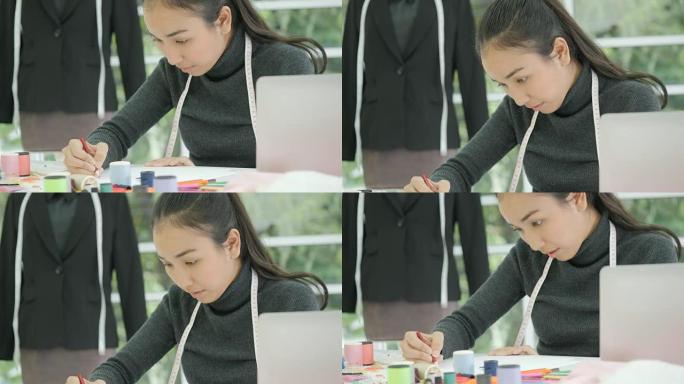 美丽的亚洲女性时装设计师坐在办公桌前看着现代工作室笔记本电脑上的草图，做笔记