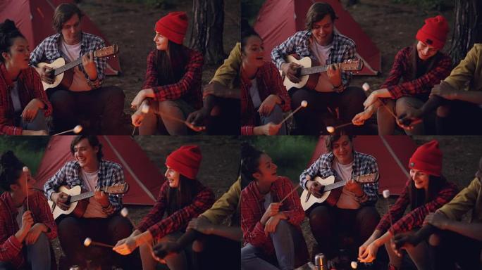 露营地的朋友在唱歌，笑着做饭，而快乐的微笑的家伙在弹吉他。露营，音乐和友谊概念。