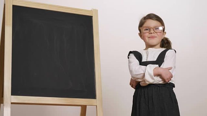 一个快乐的女孩在小黑板前打扮成老师，双臂交叉着，微笑着。