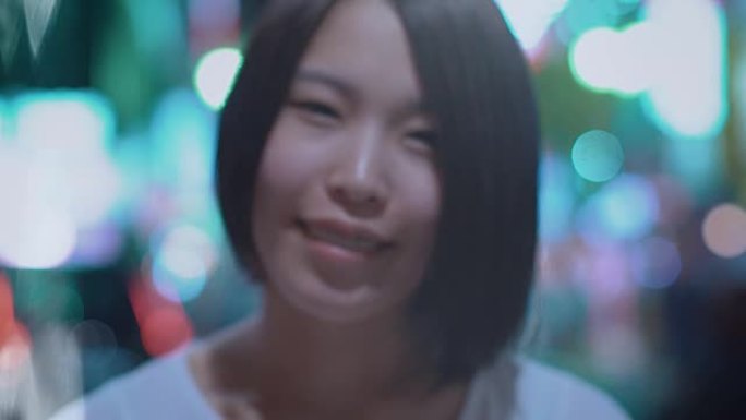 来聚焦镜头前微笑的美丽另类东亚女孩的肖像。背景中模糊的大城市灯光发光。