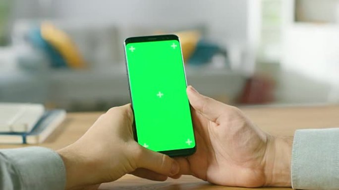 一名男子手持绿色模拟屏幕智能手机的特写镜头。使用现代高端设备。背景舒适的客厅或家庭办公室。