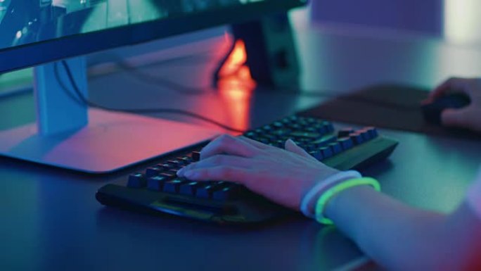 游戏玩家在键盘上玩视频游戏并使用鼠标的手的特写镜头。时尚的街机霓虹灯亮红色，粉红色，紫色，绿色。