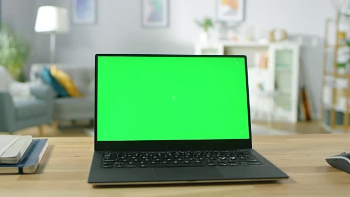 现代笔记本电脑，绿色模拟屏幕显示，站在舒适的客厅的桌子上。拿着手机的人穿过他的公寓。