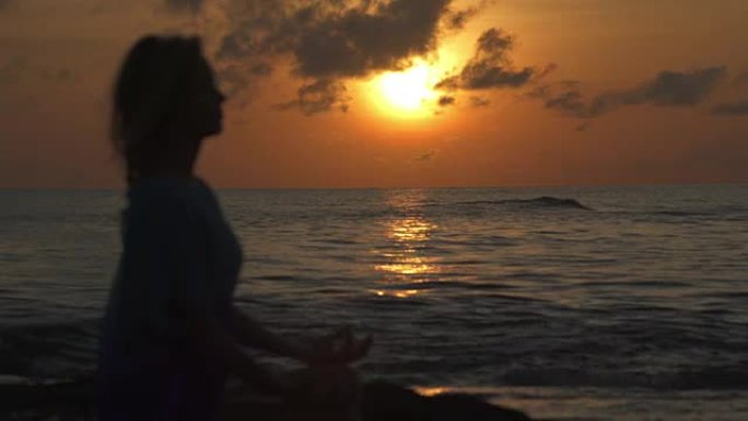 海滩上的瑜伽。以莲花姿势冥想的女人。日落