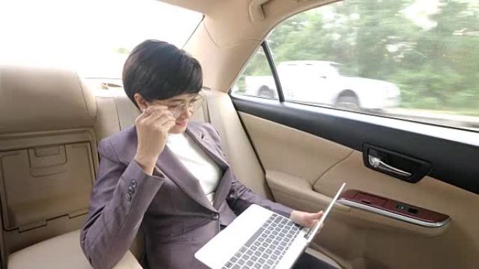 年轻迷人的亚洲女性坐在出租车的后座上，使用她的笔记本电脑