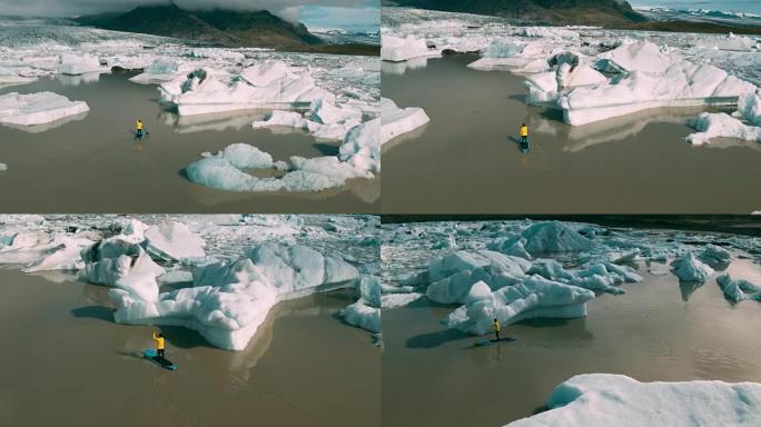 站在巨大冰山上的冰川泻湖中划桨的板子的鸟瞰图