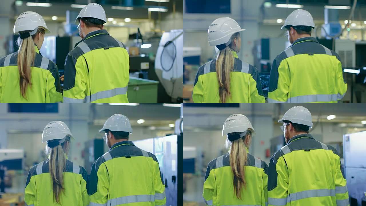 在男性和女性机械工程师交谈的镜头之后，在穿过工业工厂时，男性拿着带有发动机项目的笔记本电脑。