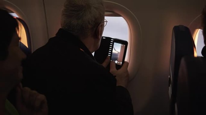无法识别的高级男性乘客试图在飞机窗户附近飞行时使用智能手机摄像头