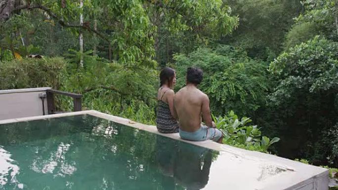种族男子坐在游泳池边的女友旁边