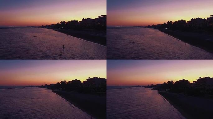 日落时游客游泳的城市海滩鸟瞰图