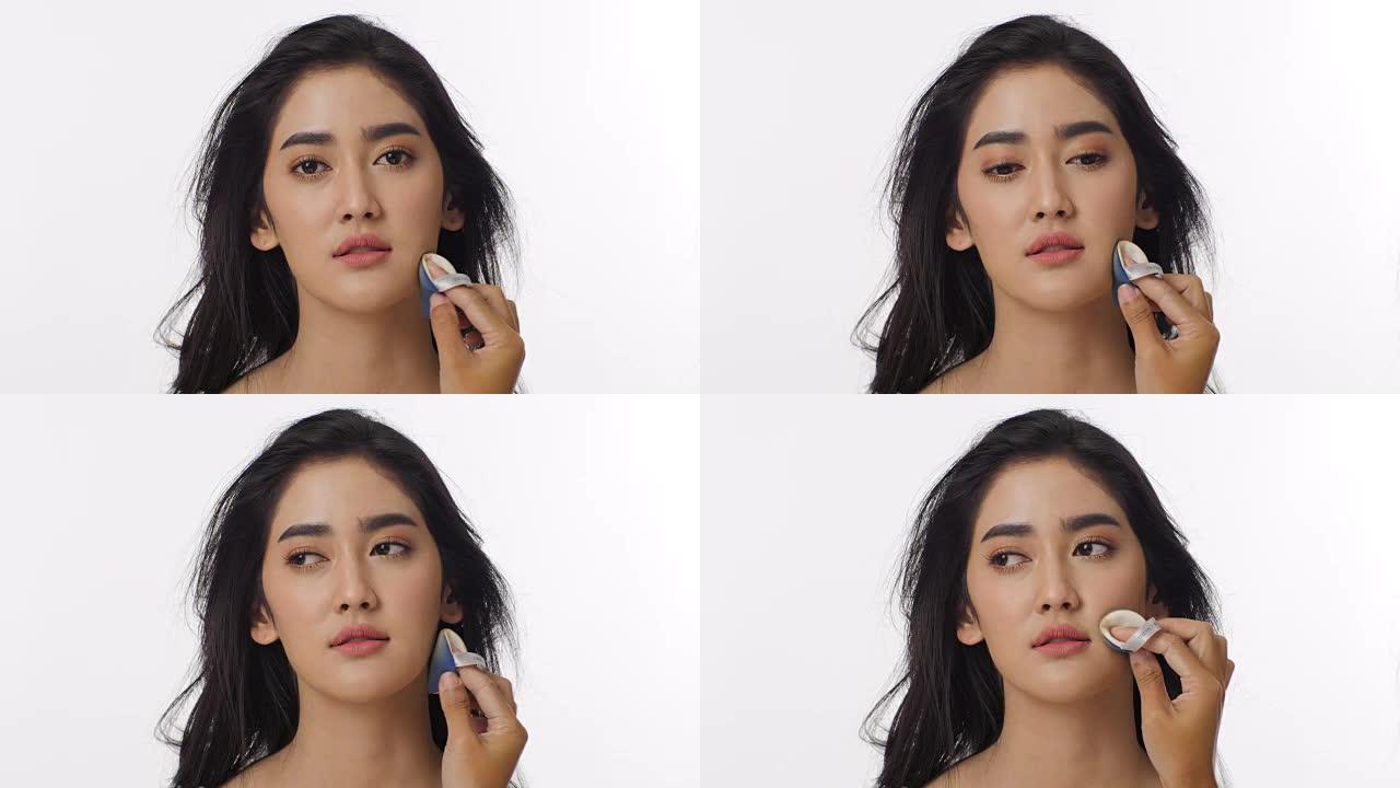 迷人的亚洲女性从专业化妆师那里化妆的特写镜头。用海绵在纯白色背景下涂抹粉底。美丽和时尚概念。