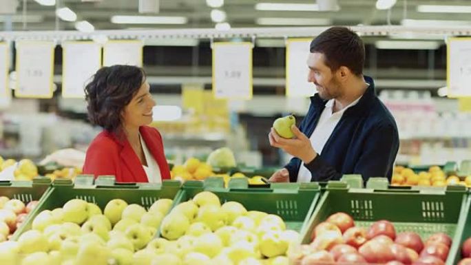 在超市: 幸福的年轻夫妇在商店的新鲜农产品区选择有机水果。丈夫使用智能手机，妻子拿起水果。